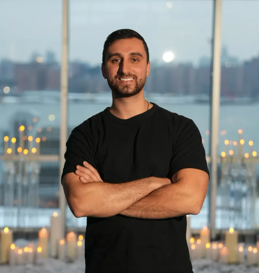 Ariel standing with his arms crossed in a black t-shirt, with candles and a city window behind him