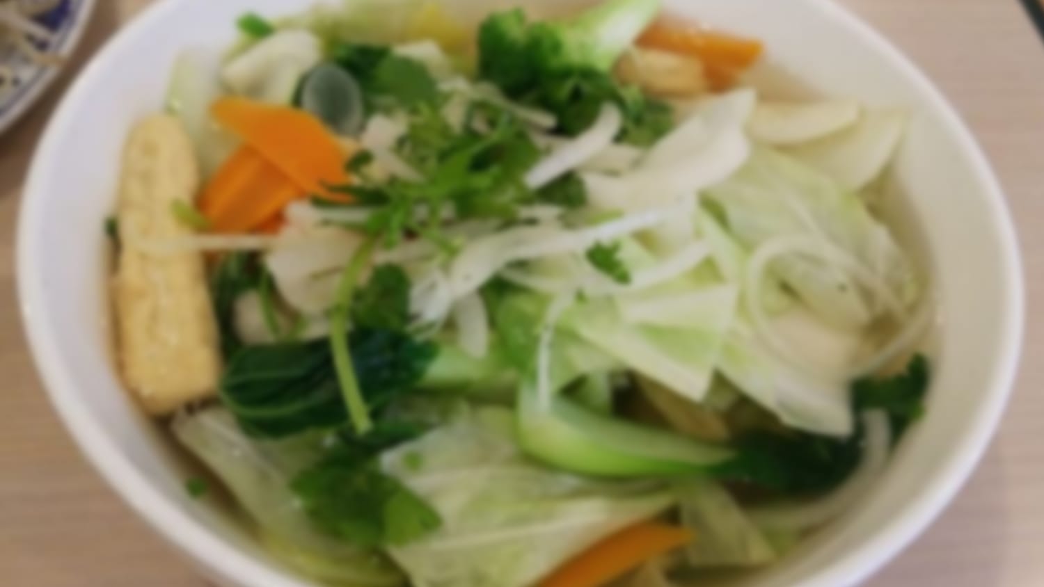 A bowl of pho topped with rare steak, fresh herbs, and lime