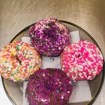 Four fancy donuts on a plate with pink, purple and rainbow sprinkles.